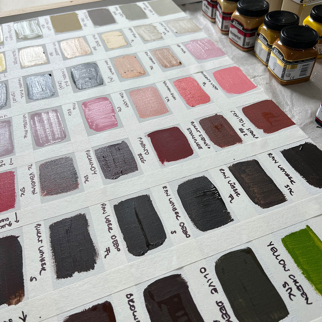 An organised display of paint swatches in various colours is shown on a canvas and several jars of Matisse Structure paint